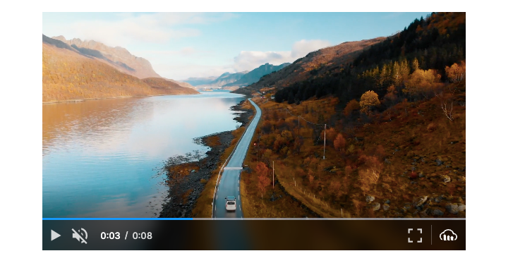 Cloudinary Video Player showing the video is on mute. The video is paused on a car driving a windy road between the mountainside on the right and a lake on the left.
