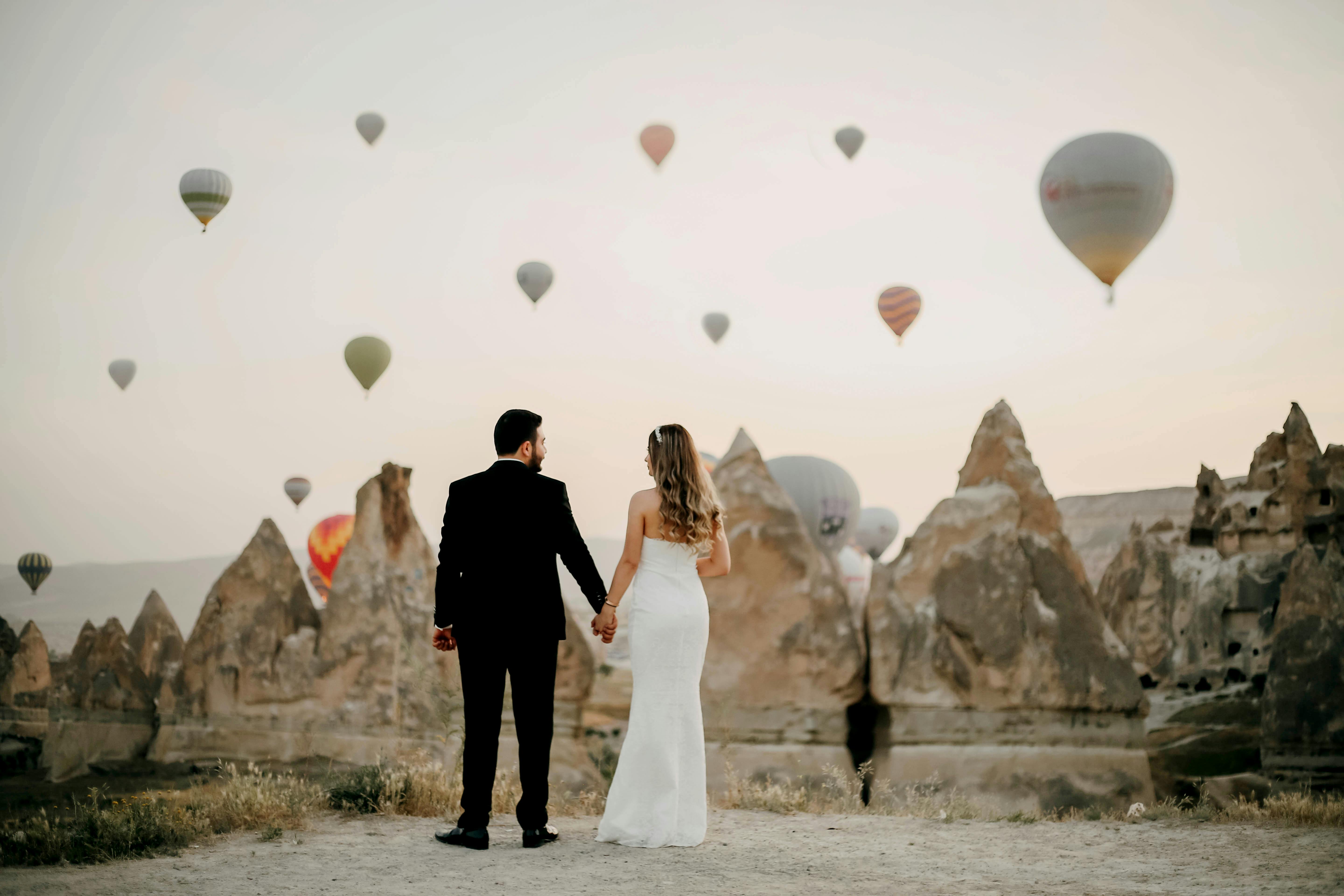 Couple holding hands in front of hot air balloons in the sky