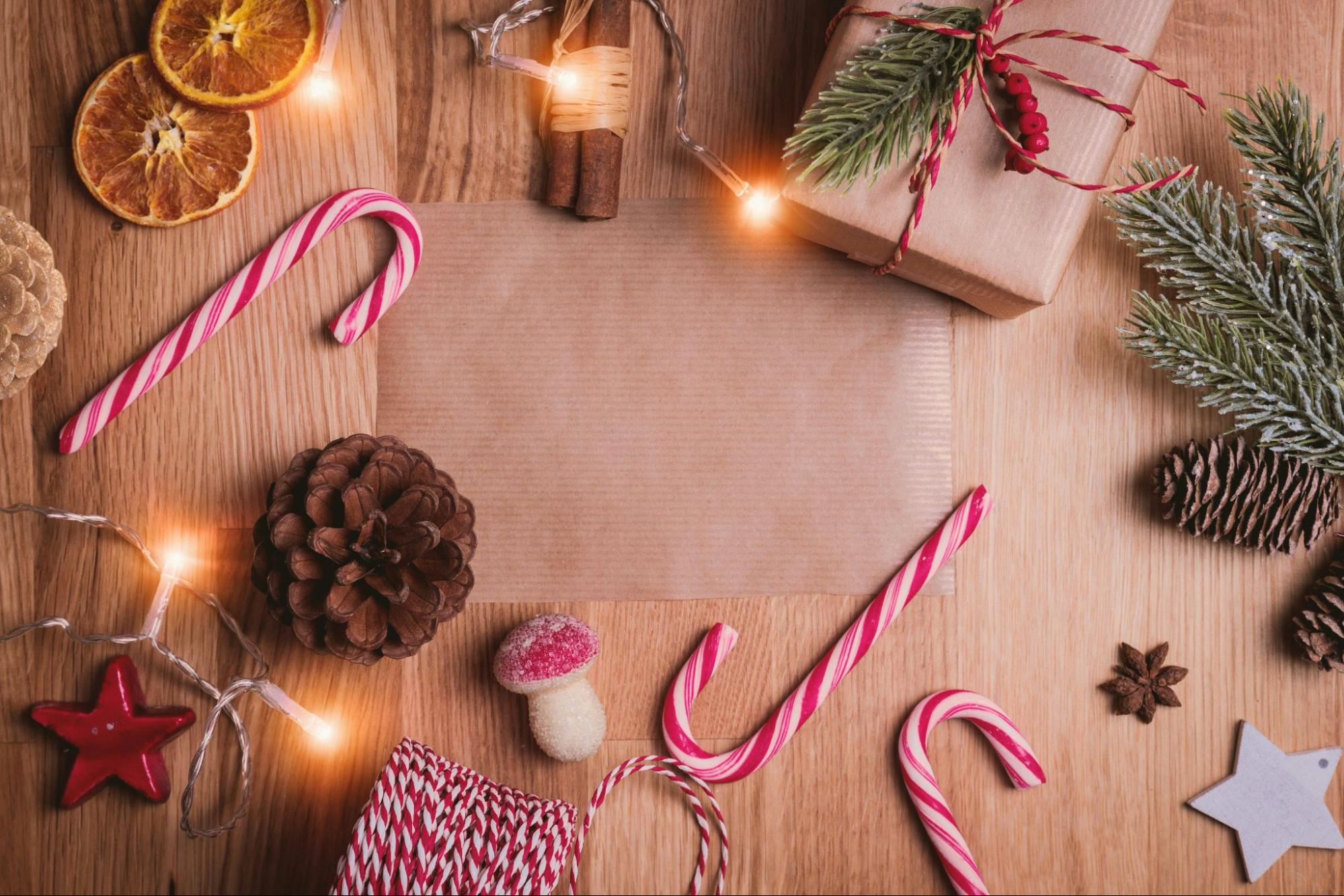 The background contains various items (candy canes, wrapped presents, dried orange slices, pinecones, and Christmas lights) on a wood floor.